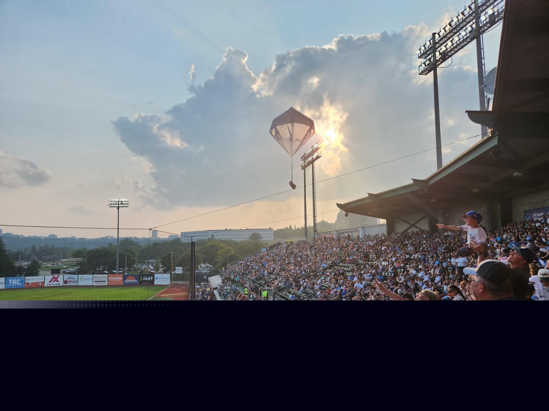Accidental Renaissance - A Hot Dog being parachuted to the waiting crowd at a baseball game with heavenly skies behind