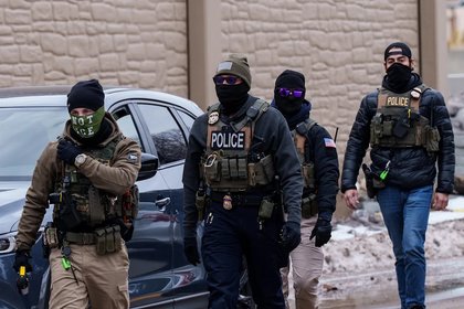 U.S. Immigration and Customs Enforcement agents, including one wearing a face covering that says 'NOT ICE,' walk near their vehicles in Richfield, Minn., on Jan. 15.