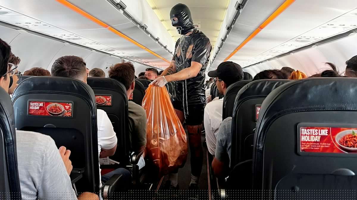 Much to the surprise of other plane passengers, man in full gimp suit helps cabin crew collect rubbish (possible nsfw content on page) [Weird]